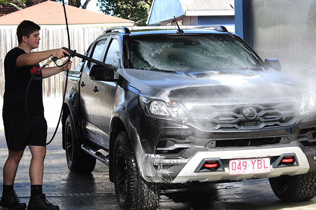 man spraying car with hose in self serve carwash bay